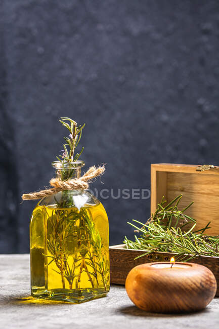 Bouteille en verre d'huile essentielle avec brindilles de romarin et bougie en bois bio brûlante sur table grise — Photo de stock