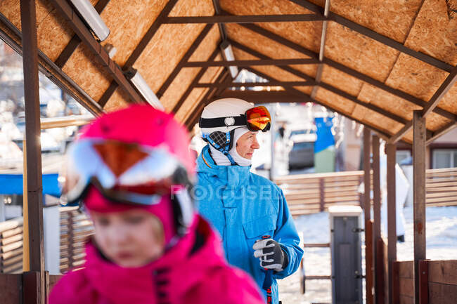 Веселый отец в лыжном шлеме и теплой спортивной одежде стоит в солнечном открытом спортивном клубе и смотрит прочь с улыбкой — стоковое фото
