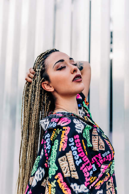 Jovem fêmea legal em roupas da moda com tranças Afro contra a parede com nervuras na cidade — Fotografia de Stock