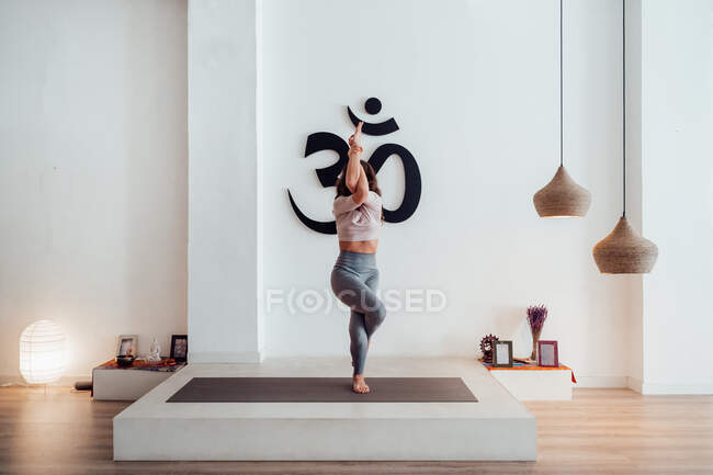 Mulher magro irreconhecível em activewear fazendo ioga no tapete em Garudasana posar em estúdio espaçoso — Fotografia de Stock