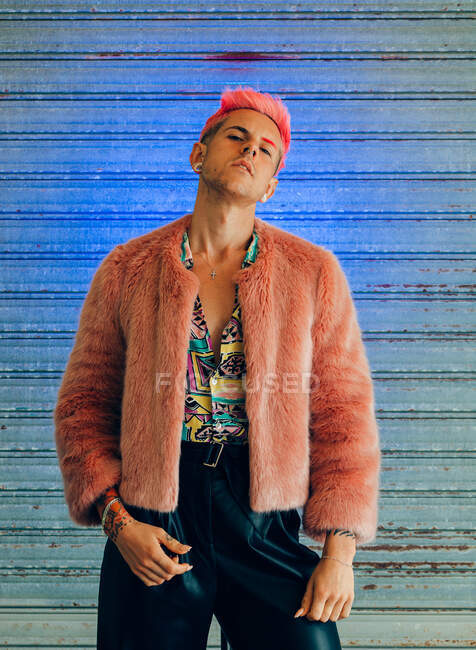Junger homosexueller Mann in modischer Kleidung mit Maniküre und modernem Haarschnitt blickt in die Kamera auf blauem Hintergrund — Stockfoto