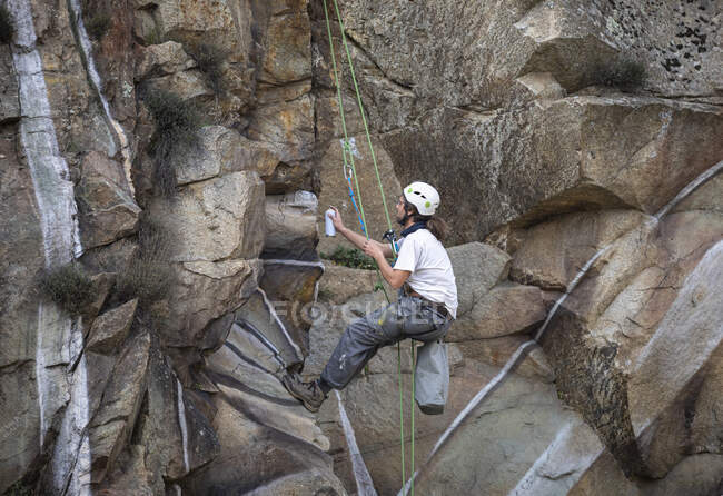 Seitenansicht Ganzkörper-Maler mit Sprühfarbe, die Graffiti am Seil am steilen Felshang hängen lässt — Stockfoto
