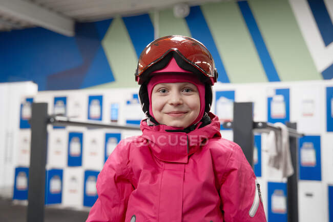 Glückliches Mädchen in rosa warmer Aktivkleidung und Helm steht im modernen Sportzentrum und blickt lächelnd in die Kamera — Stockfoto