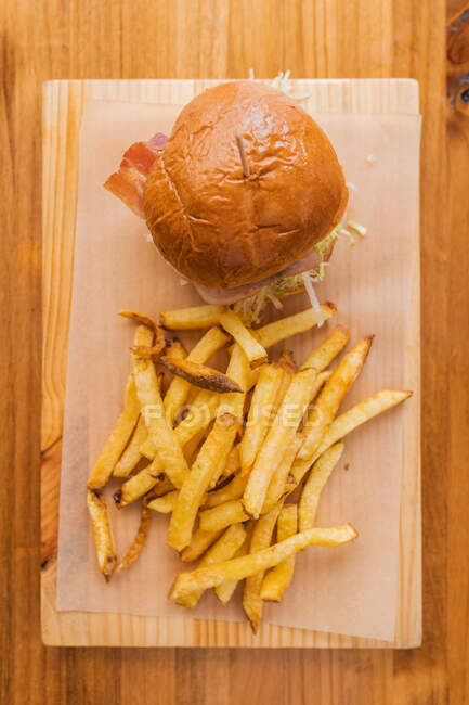 Верхній вигляд смачного свіжого гамбургера і хрусткої картоплі фрі подається на дерев'яній дошці в сучасному ресторані швидкого харчування. — стокове фото