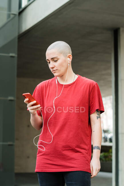 Молода гомосексуальна жінка в сорочці та навушники з мобільним телефоном дивиться на екран під час прослуховування музики — стокове фото