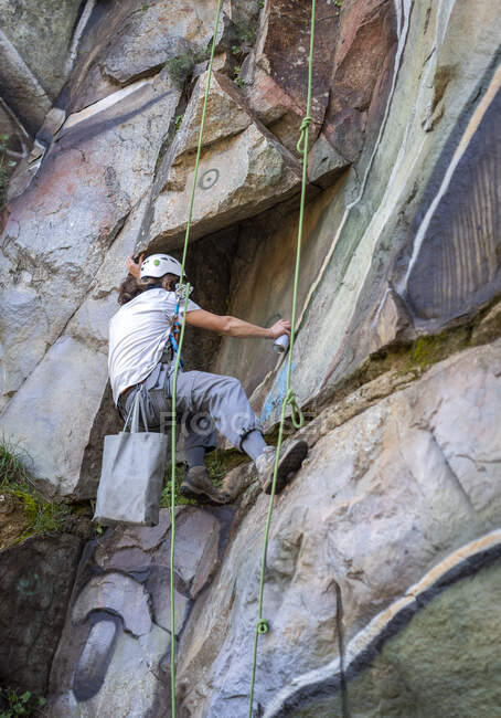 Von unten Malerin mit Sprühfarbe, die Graffiti am Seil am steilen Felshang hängen lässt — Stockfoto