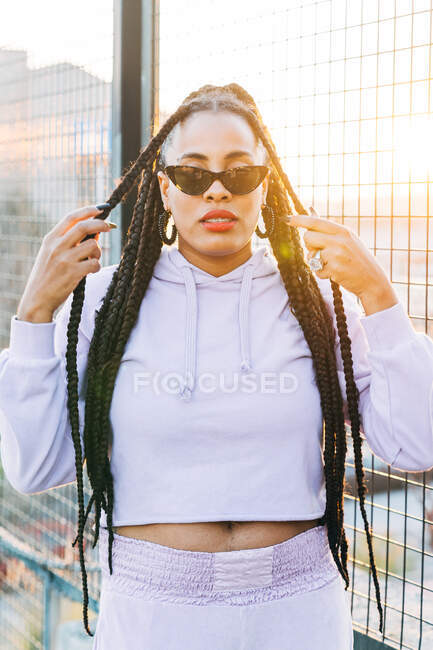Young African American female with red lips and Afro braids in sunglasses looking at camera in sunlight outdoors — Stock Photo