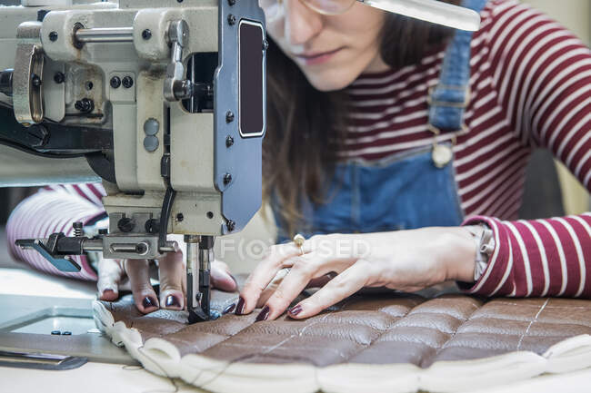 Женщина-ремесленница с помощью швейной машинки при создании обивки для мотоциклетного кресла в мастерской — стоковое фото