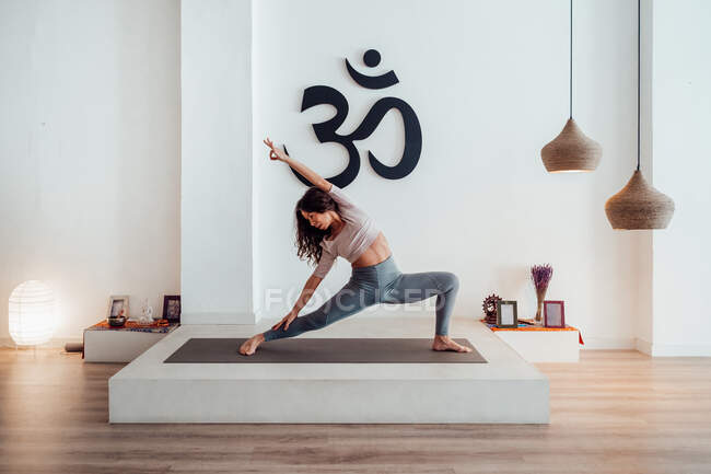 Sottile donna in abbigliamento sportivo pratica yoga in Parsvakonasana sul tappeto in studio e stretching corpo — Foto stock