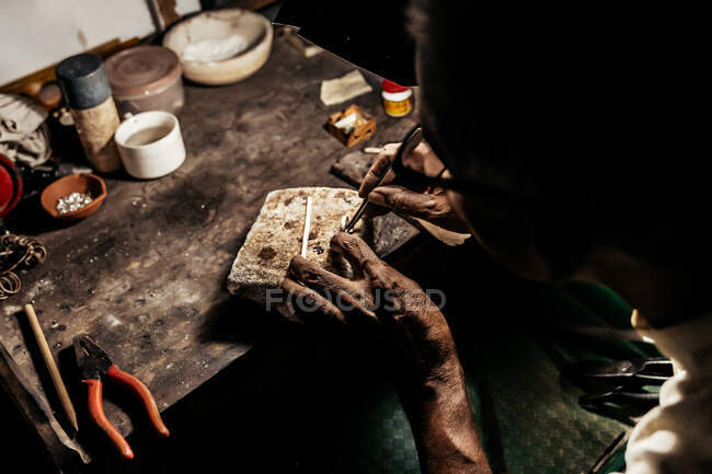 From above cropped anonymous mature ethnic man working at weathered desk in craft workshop — Stock Photo
