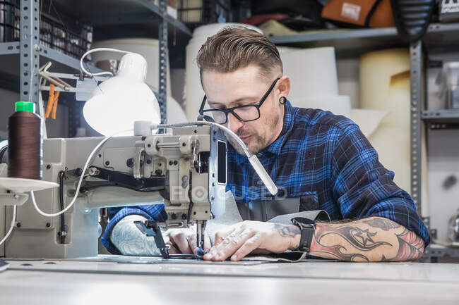 Male artisan using sewing machine while creating upholstery for motorbike seat in workshop — Stock Photo