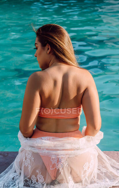 Back view of anonymous plump female tourist in swimwear with sitting against swimming pool during vacation — Stock Photo