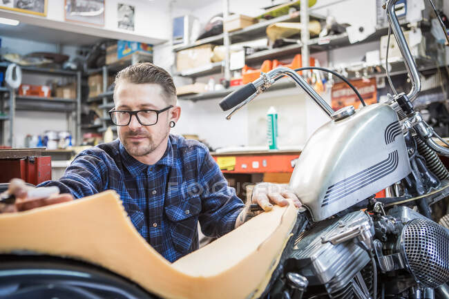 Busy bearded craftsman using foam rubber for creating handmade motorcycle seat in workshop — Stock Photo
