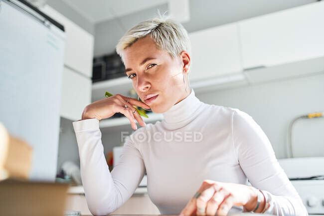 Crop adult female astrologist with makeup touching face and chin while looking at camera in house — Stock Photo