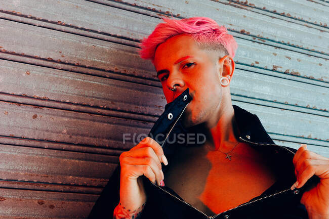 Homem homossexual jovem com tatuagem e cabelo rosa em outerwear elegante olhando para a câmera contra a parede resistida — Fotografia de Stock