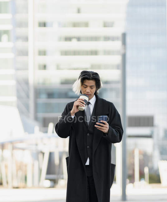 Jovem bem vestido executivo masculino étnico com celular e bebida quente para ir na cidade — Fotografia de Stock