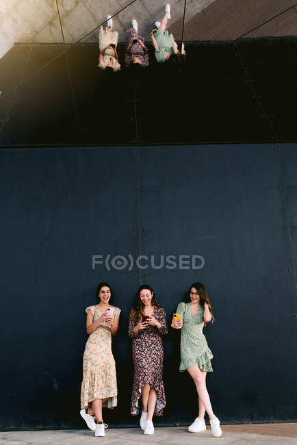 Conteúdo Jovens melhores amigas em roupas da moda com celulares em pé na passarela urbana contra a parede — Fotografia de Stock