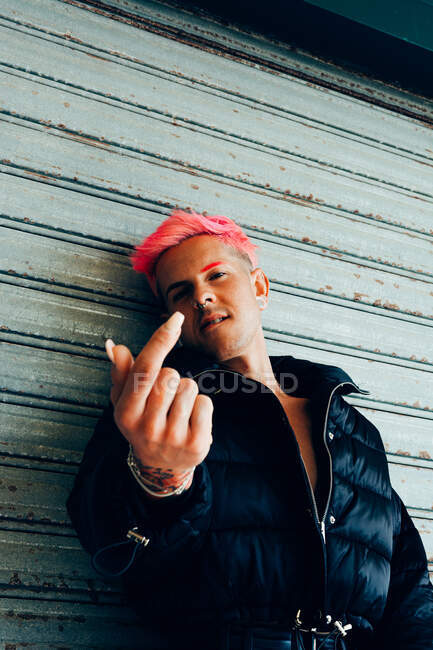 Trendy homosexual man in padded jacket with pink hair showing nail while looking at camera — Stock Photo