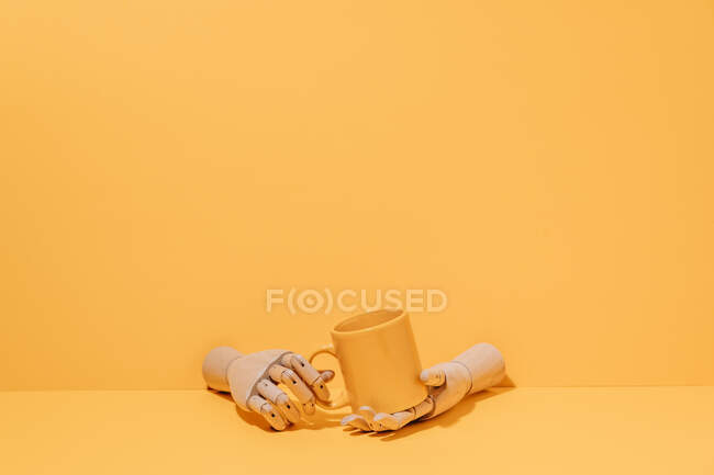 Creativo ornamentale in legno mano tenendo tazza colorata su sfondo giallo in studio — Foto stock