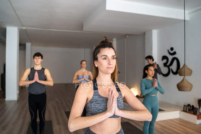 Mujer serena en ropa deportiva de pie en la montaña con las manos de oración posan y hacen yoga durante la clase de grupo en el estudio - foto de stock