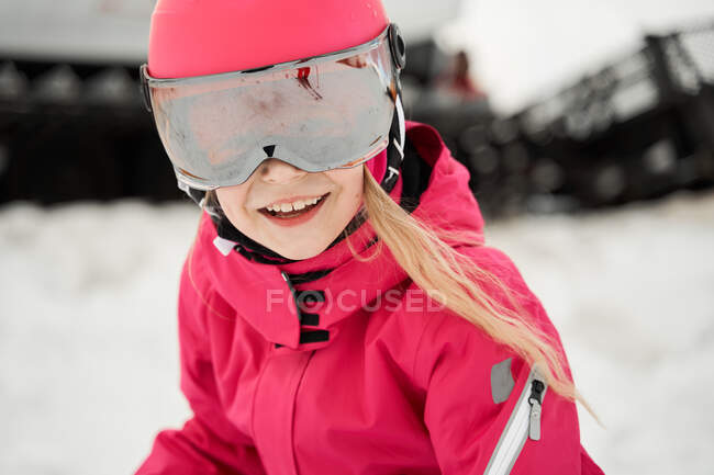 Positive cute girl in pink warm activewear goggles and helmet skiing alongside snowy slope on clear winter day — Stock Photo