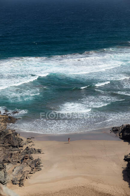 From above back view of anonymous female traveler admiring foamy ocean from sandy beach between mountains — Stock Photo