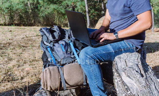 Side view of anonymous nomad sitting on stone near belongings and using netbook while working remotely — Stock Photo