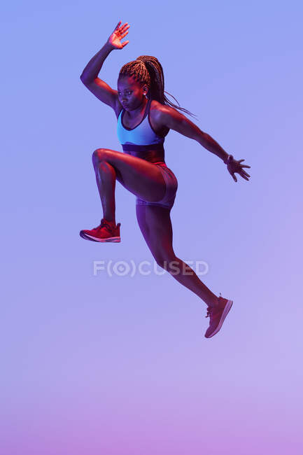 Vue latérale d'une sportive afro-américaine déterminée sautant avec des cheveux volants tout en regardant vers l'avant pendant l'entraînement cardio — Photo de stock