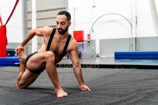 Masculino étnico enfocado muscular de cuerpo completo en pantalones cortos deportivos que realizan Twisted Monkey Pose mientras practican yoga en un moderno gimnasio - foto de stock