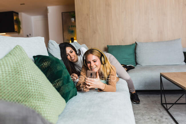 Casal de mulheres lésbicas deitadas no sofá e tomando auto-tiro no smartphone enquanto relaxam juntas na sala de estar no fim de semana — Fotografia de Stock