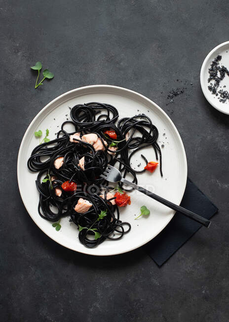 From above black ink spaghetti with salmon in ceramic plate on dark background — Stock Photo