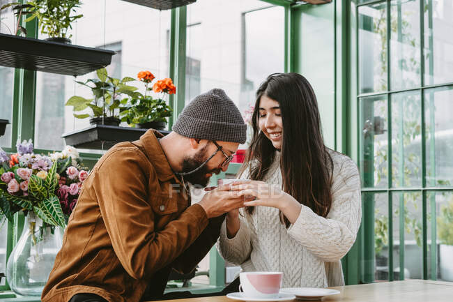 Couple in love drinking hot beverages while sitting at table in cafe with flowers — Stock Photo