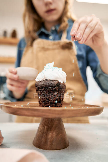 Анонимные урожая женщин украшения вкусный шоколадный кекс на торт стенд с сахаром посыпать во время приготовления пищи на кухне — стоковое фото