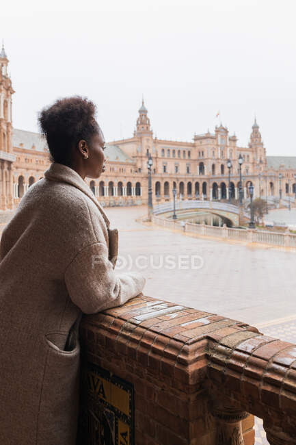 Giovane donna afroamericana in abbigliamento casual ammirare viste del grande palazzo con colonnato stucco ornamenti di lavoro e colonne durante la visita Siviglia Spagna — Foto stock