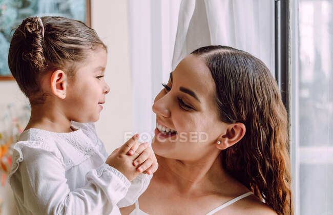 Вид етнічної матері з милою маленькою донькою, яка дивиться один на одного, стоячи вдома. — стокове фото