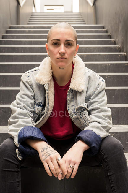 Junge transsexuelle Person in lässiger Kleidung sitzt auf einer Treppe zwischen Häuserwänden und blickt in die Kamera — Stockfoto