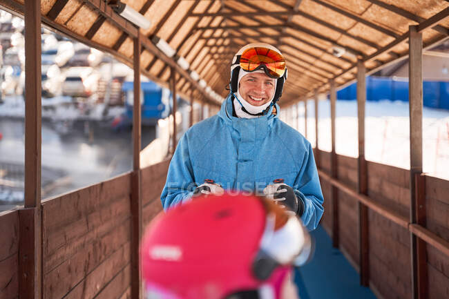 Allegro padre con casco da sci e caldo abbigliamento sportivo in piedi nel soleggiato club sportivo all'aperto e guardando la fotocamera con sorriso — Foto stock