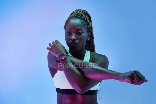 Молодая афроамериканская спортсменка в спортивной одежде тренируется, отводя взгляд на синий фон — стоковое фото