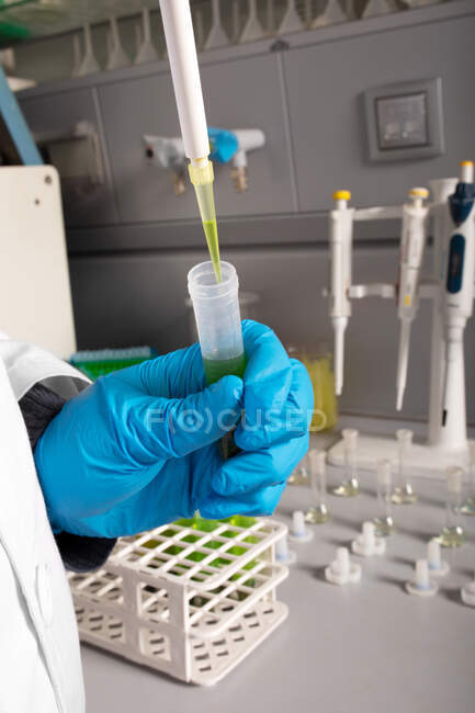 Químico anónimo de cultivo vertiendo aceite de marihuana de pipeta en tubo de muestra durante el examen en laboratorio - foto de stock