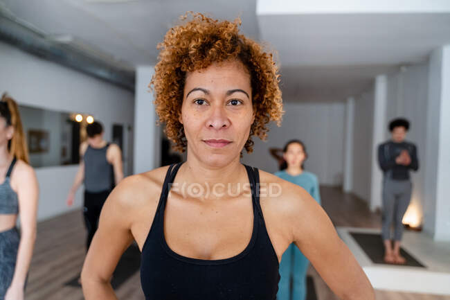 Zufriedene Frau mit Afro-Frisur steht während des Yoga-Kurses im geräumigen Studio mit verschiedenen Leuten — Stockfoto