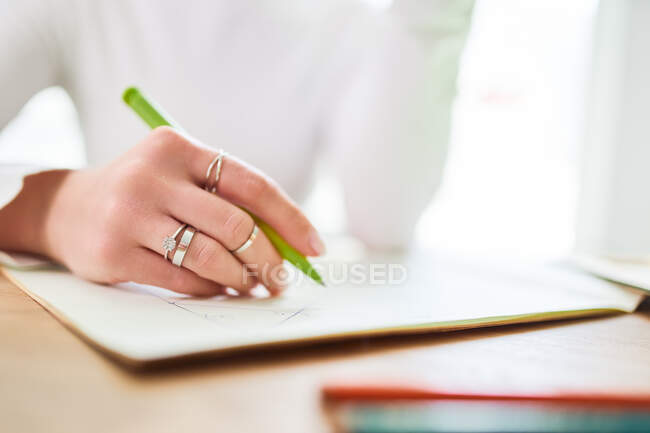Crop of anonymous female astrologist taking notes in notepad at desk at home in sunlight — Photo de stock