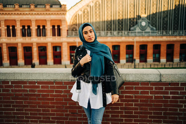 Content ethnic female in traditional hijab and trendy clothes standing on city street and looking at camera — Stock Photo