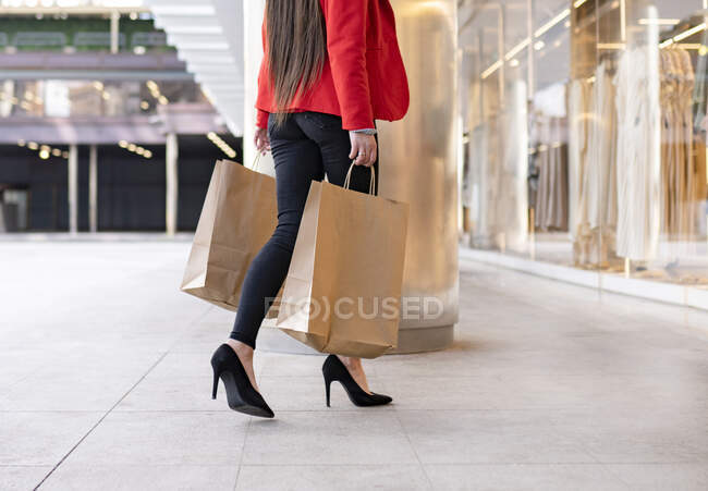 Cultivez acheteur féminin avec des sacs à provisions en papier et café à emporter debout près de vitrine du magasin en ville — Photo de stock