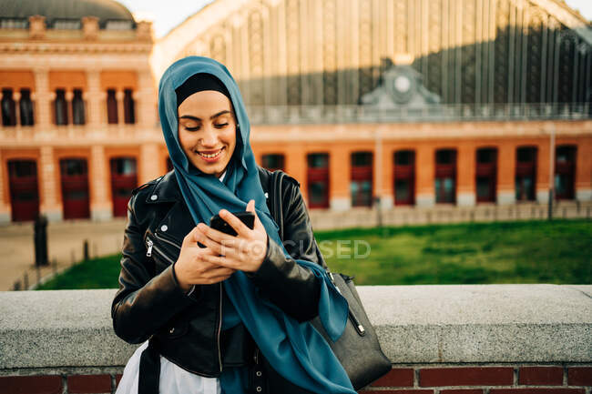 Muslim female in traditional headscarf standing on city street and browsing phone — Stock Photo