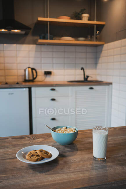 Plate with tasty oatmeal biscuits with chocolate chips against glass of milk on wooden table — Stock Photo