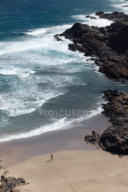 De cima vista traseira do viajante fêmea anônimo admirando o oceano espumoso da praia arenosa entre montanhas — Fotografia de Stock