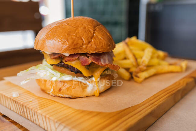 Köstliche frische Hamburger und knusprige Pommes frites auf Holzbrett im modernen Fast-Food-Restaurant serviert — Stockfoto