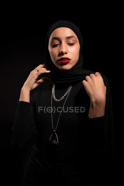 Atractiva joven mujer islámica con traje negro y hijab suavemente mirando hacia abajo - foto de stock