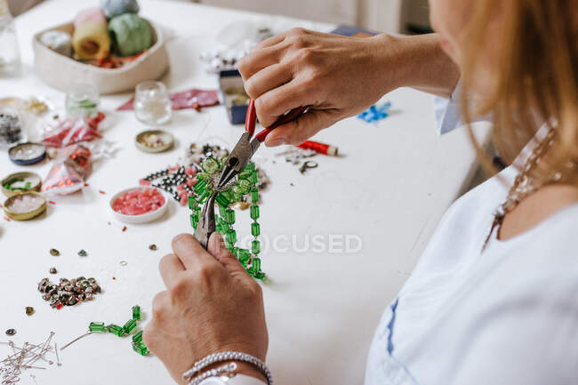 High angle of crop anonymous female master with instrument making necklace at table with different tools — Stock Photo