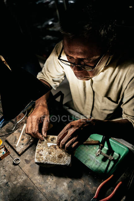 D'en haut homme ethnique mature travaillant à un bureau altéré dans un atelier artisanal — Photo de stock